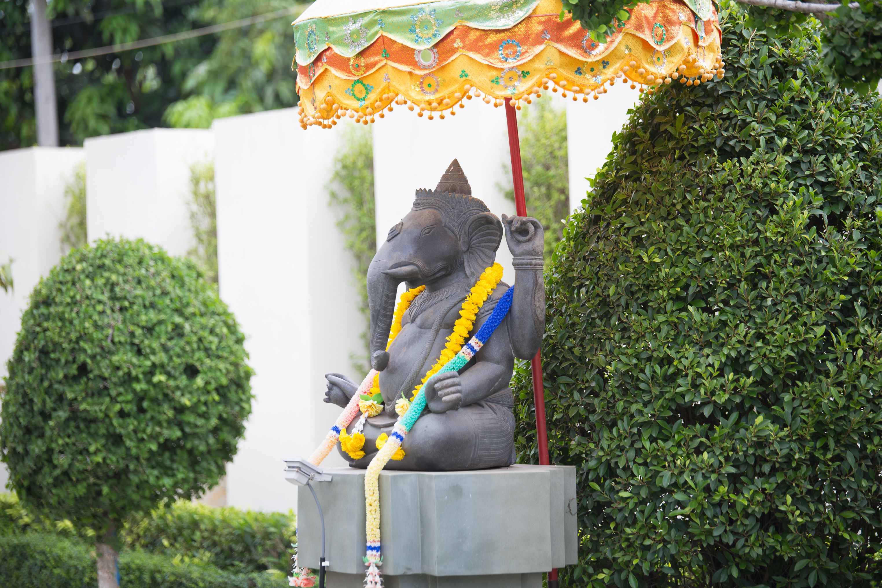Una estatua de una deidad con forma de elefante, con un toldo colorido, rodeada de arbustos cuidadosamente podados.