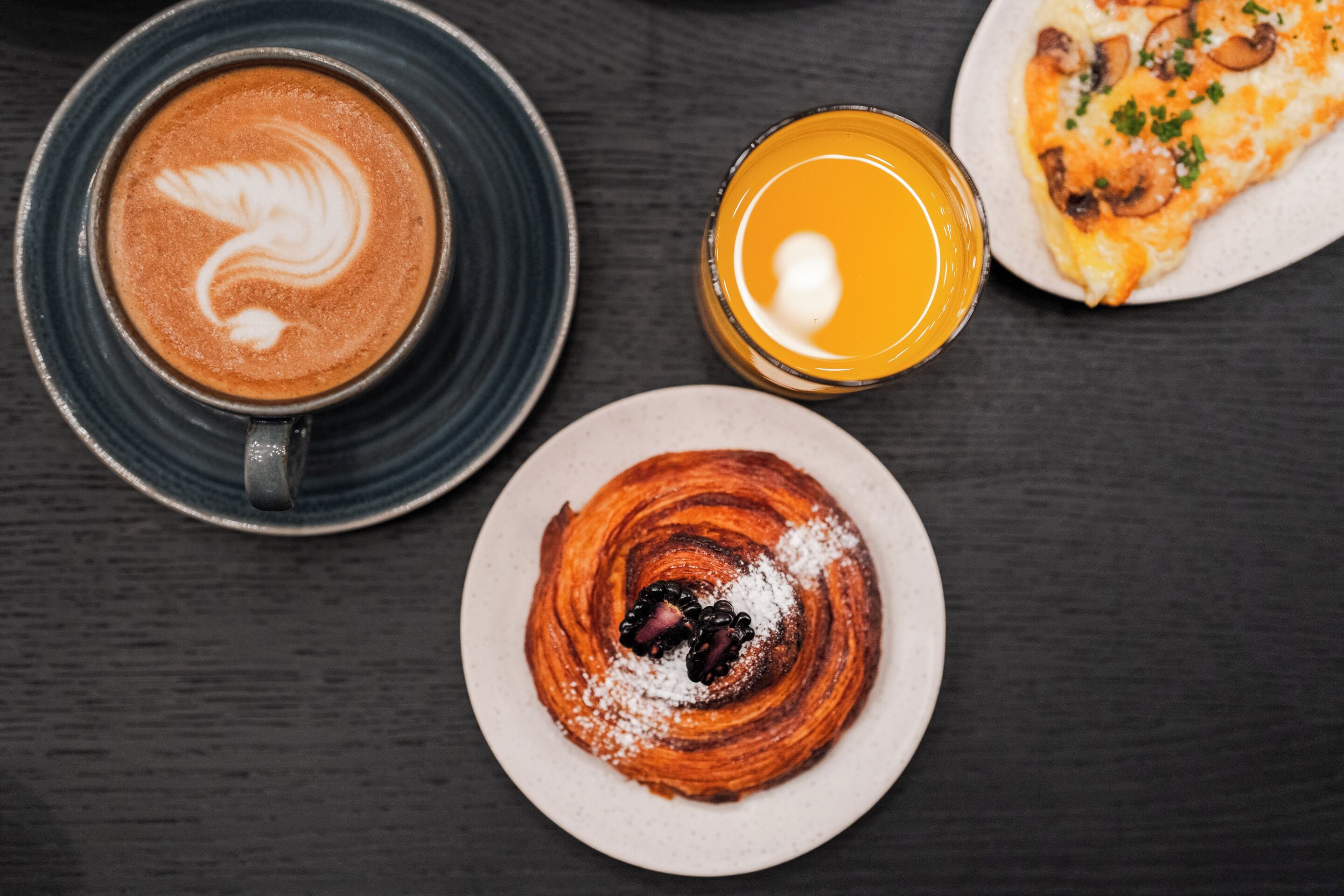 A table with a coffee cup, a glass of orange juice, a plate with a pastry, and a pizza.