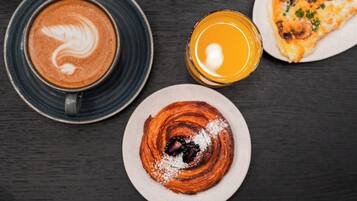 A table with a coffee cup, a glass of orange juice, a plate with a pastry, and a pizza.