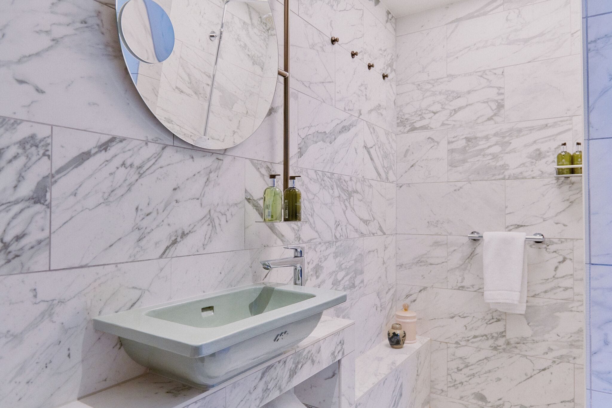 Un baño con pared de mármol, un lavabo rectangular, un espejo y un perchero para toallas.