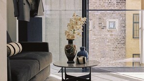 A modern living room with a sofa, a table with a vase, and a suit on a mannequin.