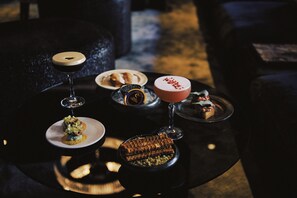 A table with various food items and drinks, including a dessert, a cocktail, and a beverage in a bottle.