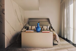 A bedroom with a bed, a bedside table with books, a blue vase, and a window with curtains.
