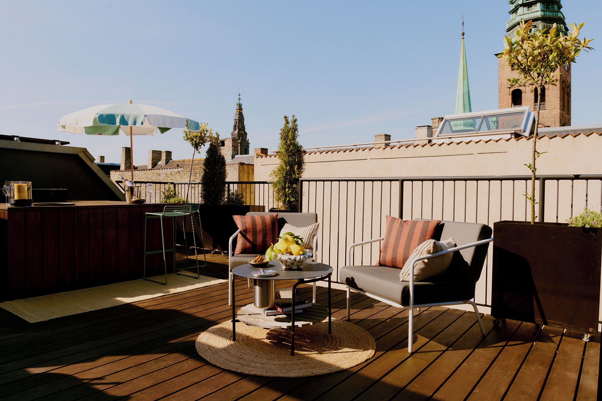 Een terras op het dak met buitenmeubels, een barbecue en uitzicht op een kerktoren.