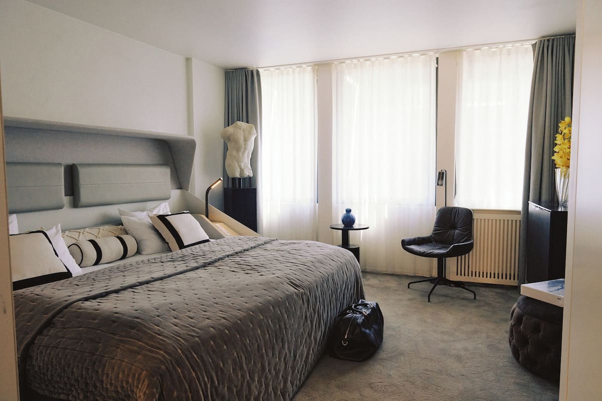 Ett hotellrum med en säng, en stol, ett litet bord och ett element.