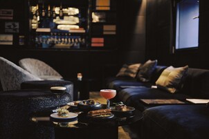 A dimly lit lounge area with a bar, sofas, and a small table with drinks and snacks.