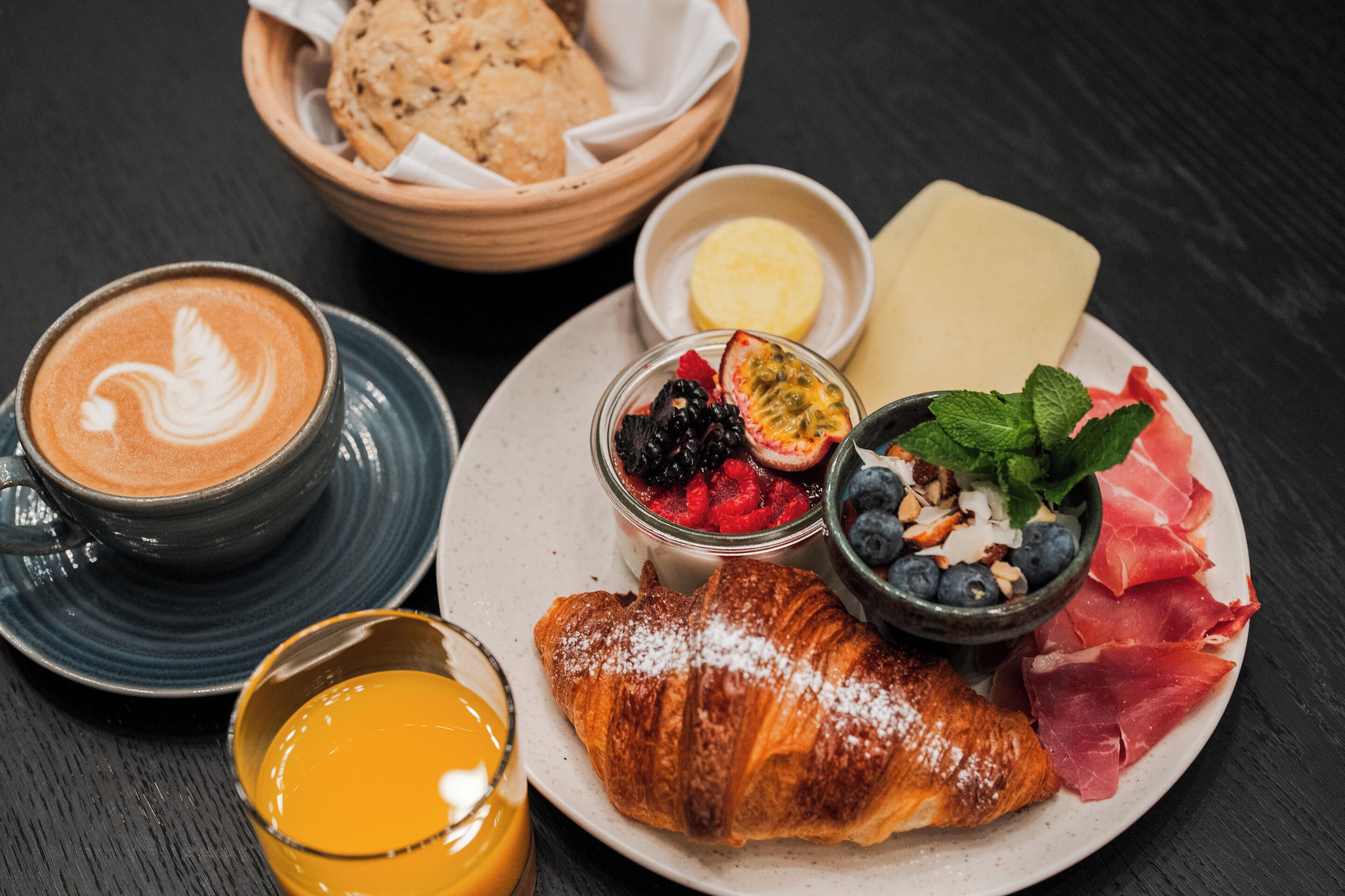 Een bord met een croissant, fruit, kaas en een kop koffie.