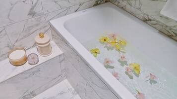 Una bañera con diseños florales, suelo de baldosas de mármol y estante con velas y un recipiente.