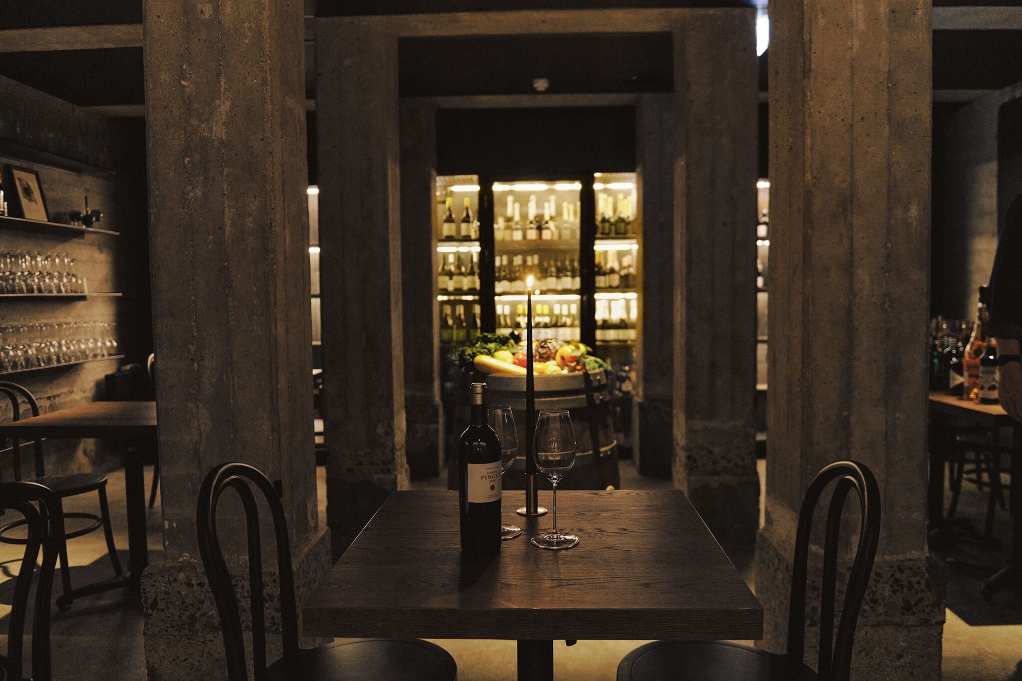 Een restaurantinterieur met een bar, eettafels en een wijnrek op de achtergrond.