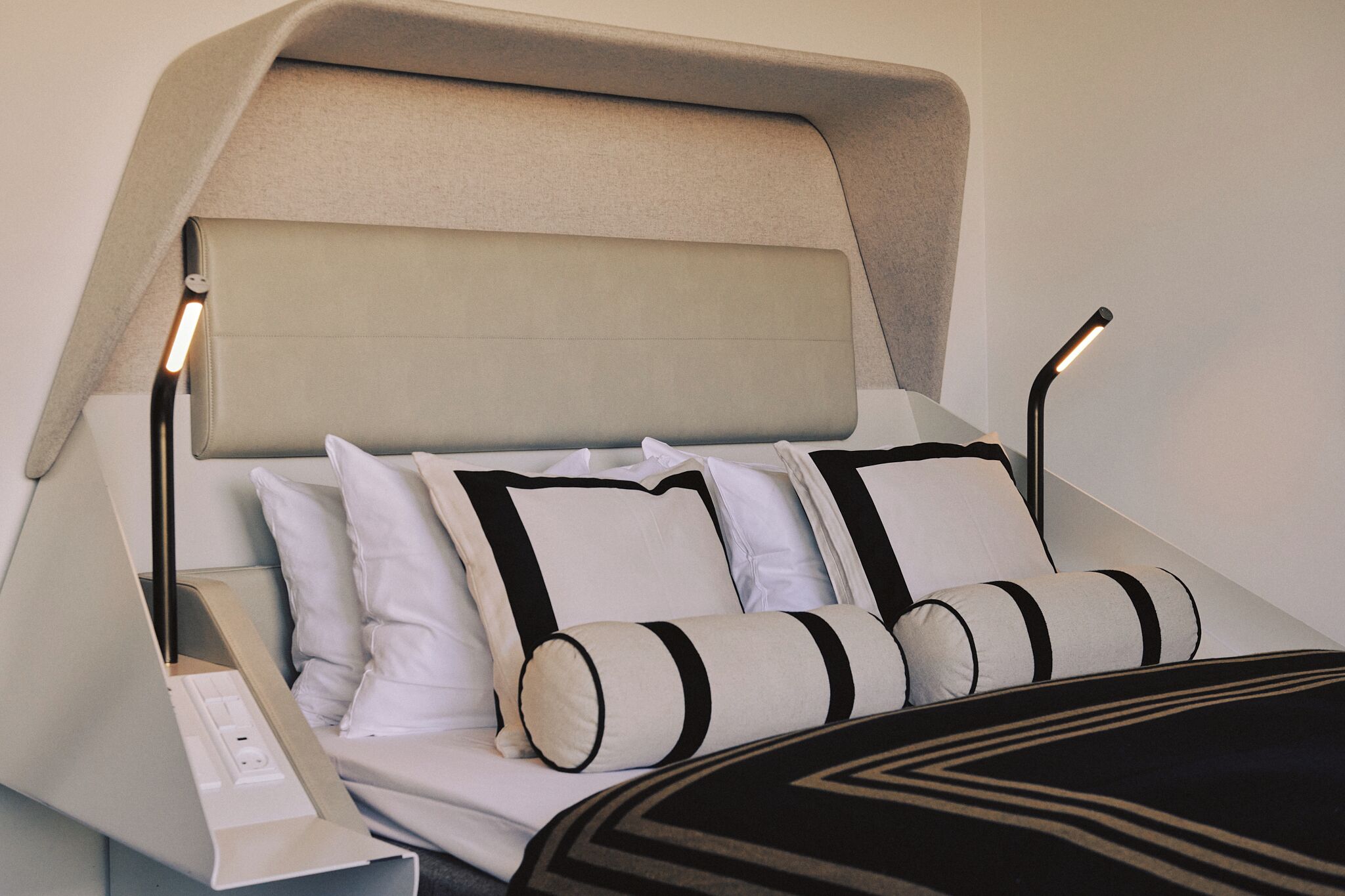 Uma cama moderna com cabeceira, roupa de cama branca e mesa de cabeceira com abajur.