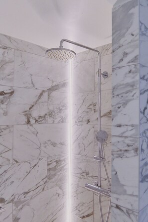 A shower with a rain showerhead and handheld showerhead, set against marble walls. - Boutique Hotel Herman K (Copenhagen)