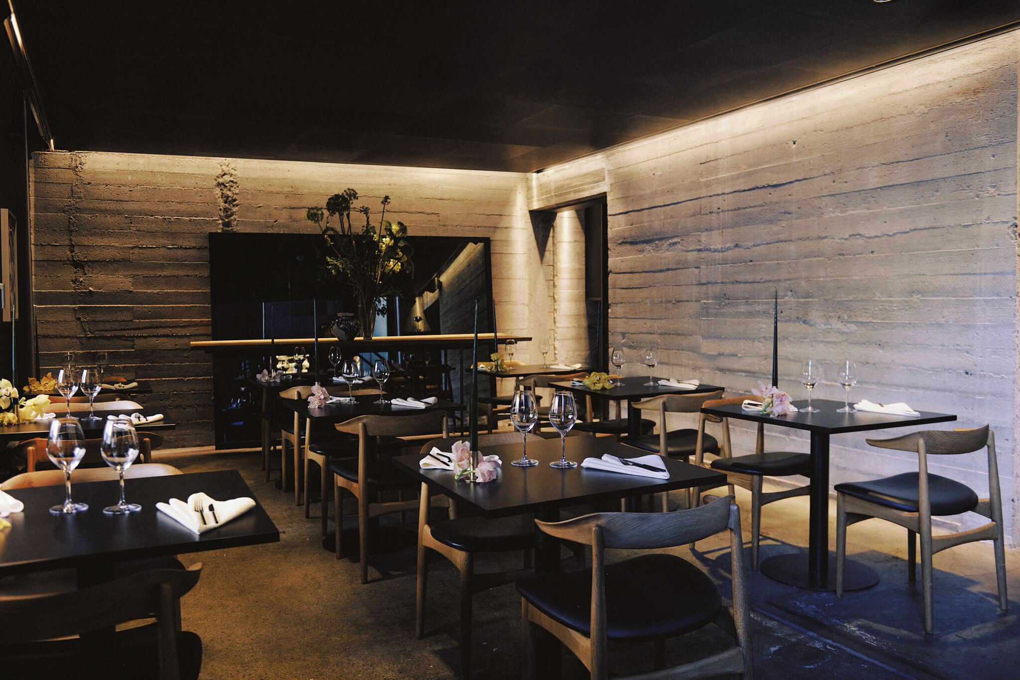 Un restaurante con paredes de madera, mesas dispuestas con copas de vino y sillas.