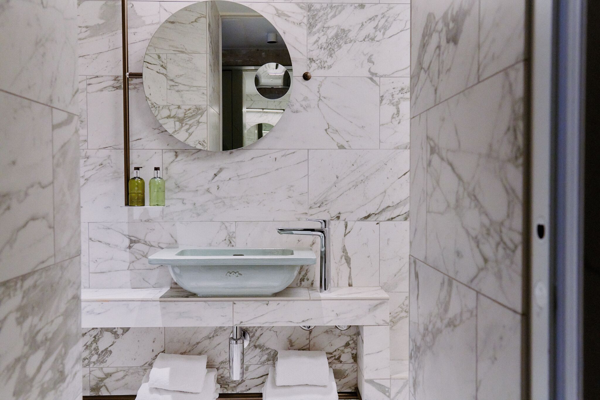 Un baño con lavamanos de mármol, espejo y toallero.