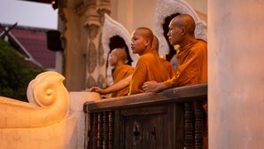 Des moines vêtus de robes orange sont assis devant un pupitre en bois, une statuette sculptée se trouvant devant eux.