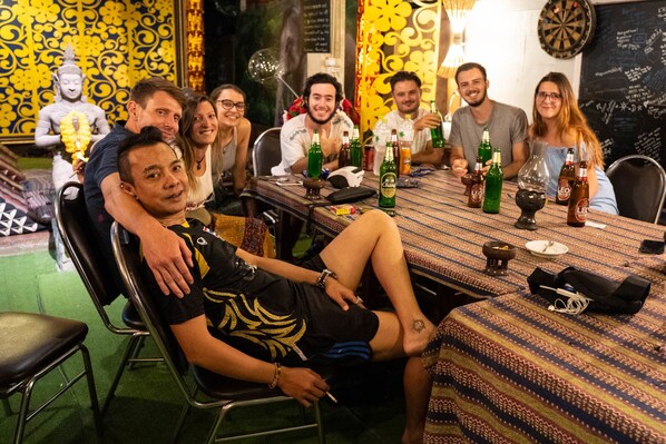 A group of people seated around a table with bottles and glasses, in a room with patterned wallpaper and a Buddha statue. - Thailand wow Guesthouse - Hostel - Adults Only (Chiang Mai)
