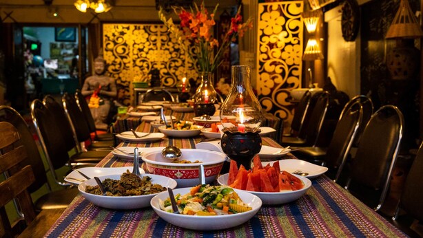 Un restaurant où une longue table est dressée pour un repas, avec différents plats et un chandelier allumé en guise de décoration centrale.