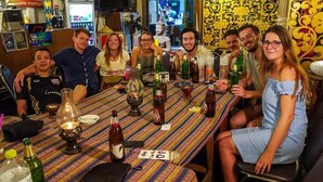 Un groupe de personnes est assis autour d’une table, devant différentes bouteilles et différents verres, ce qui suggère qu’il s’agit d’un rassemblement convivial.