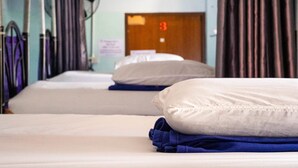 Une chambre d’hôtel avec deux lits, chacun muni d’un oreiller et d’une serviette bleue pliée. On aperçoit une porte portant le numéro « 3 » à l’arrière-plan.