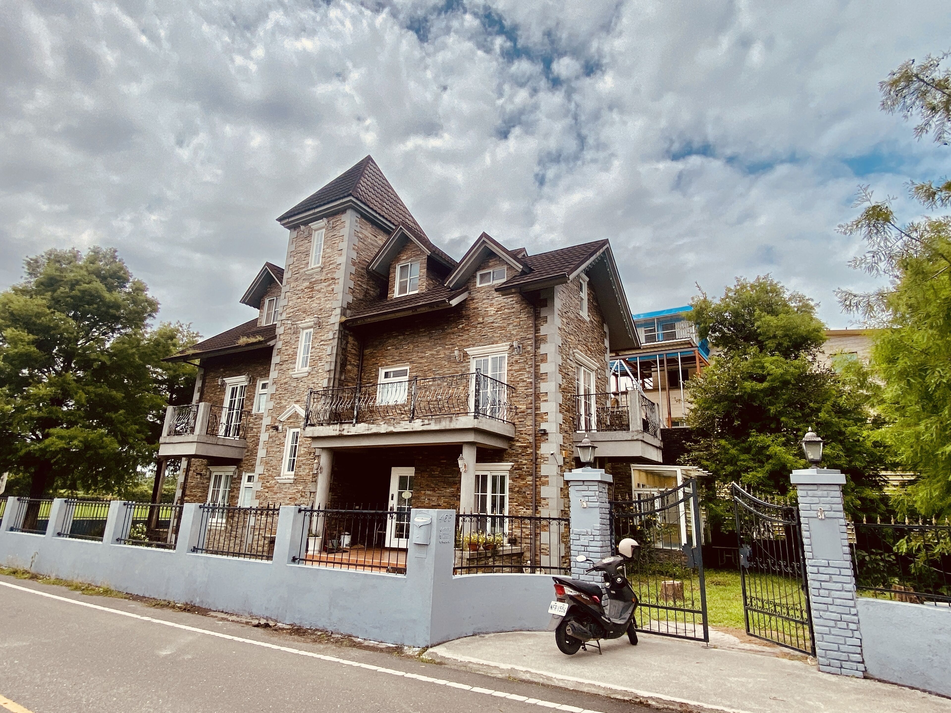 Une grande maison à plusieurs étages, dotée d’une façade en pierre, de nombreux balcons et d’une entrée fermée par un portail.