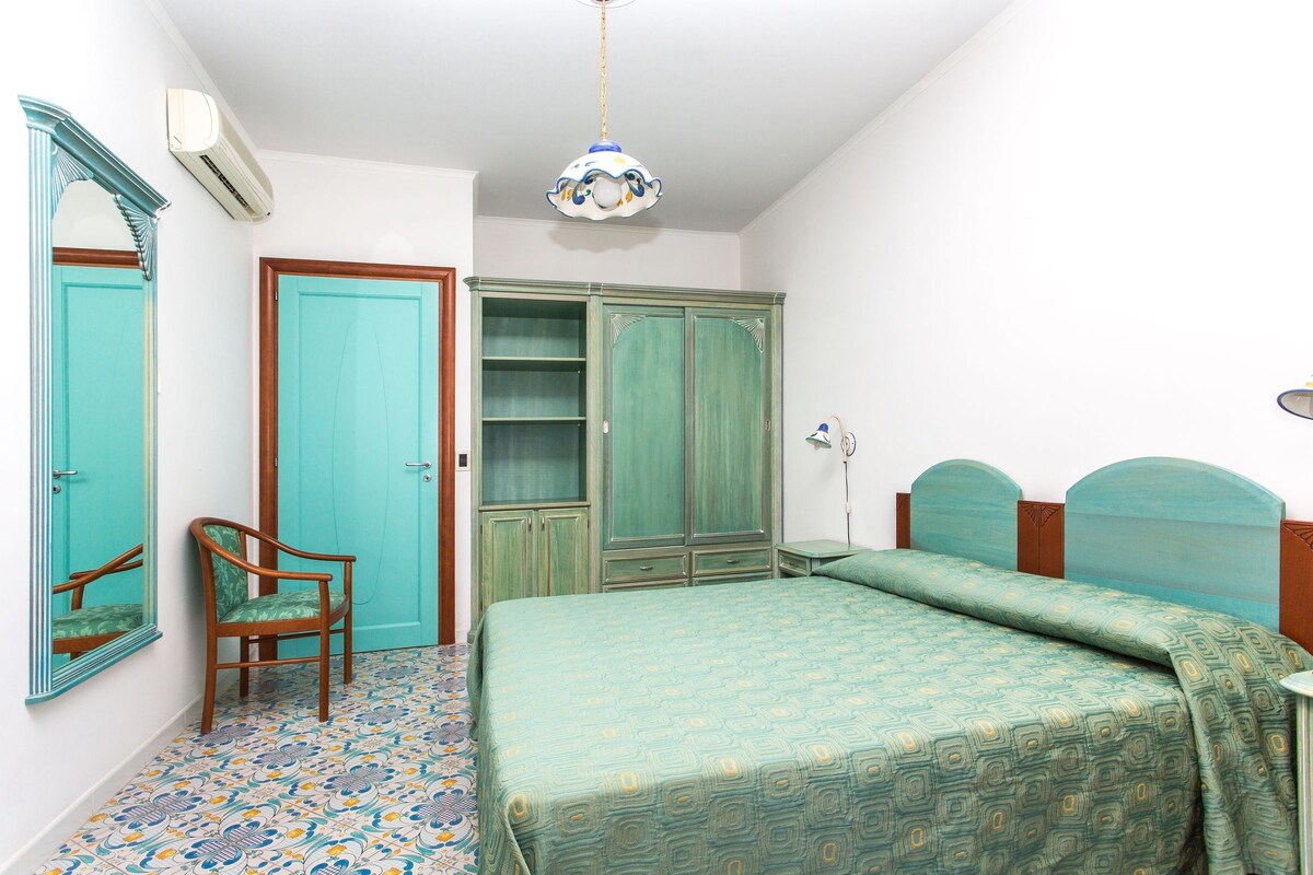 A bedroom with a bed, a chair, a wardrobe, and a mirror.