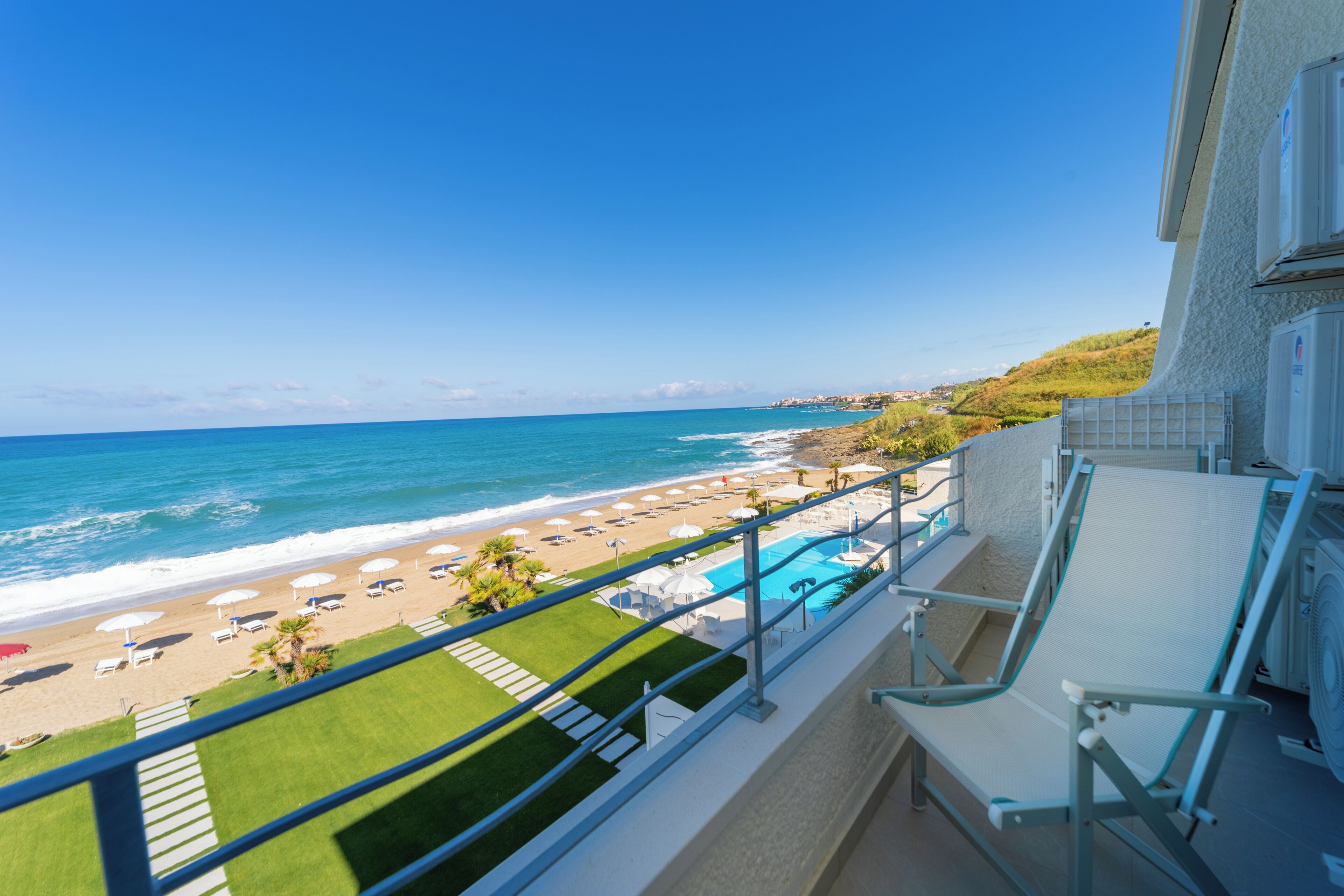 A balcony with a view of the beach, a pool, and a clear blue sky.