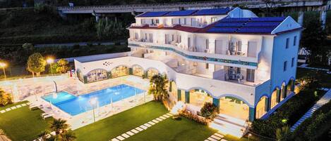 Un edificio grande de varios pisos con piscina, varios balcones y un césped cuidado.