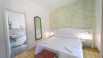 Une chambre d’hôtel comprenant un lit, une table de chevet, une commode, un miroir et une salle de bain avec un lavabo et un miroir.