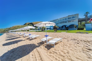 A beach with sun loungers and umbrellas, a building with a balcony, and a clear blue sky. - Hotel Poseidon (Belvedere Marittimo)