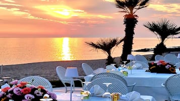 Une vue sur le coucher de soleil, avec des tables dressées pour le dîner, des palmiers et une plage en arrière-plan.