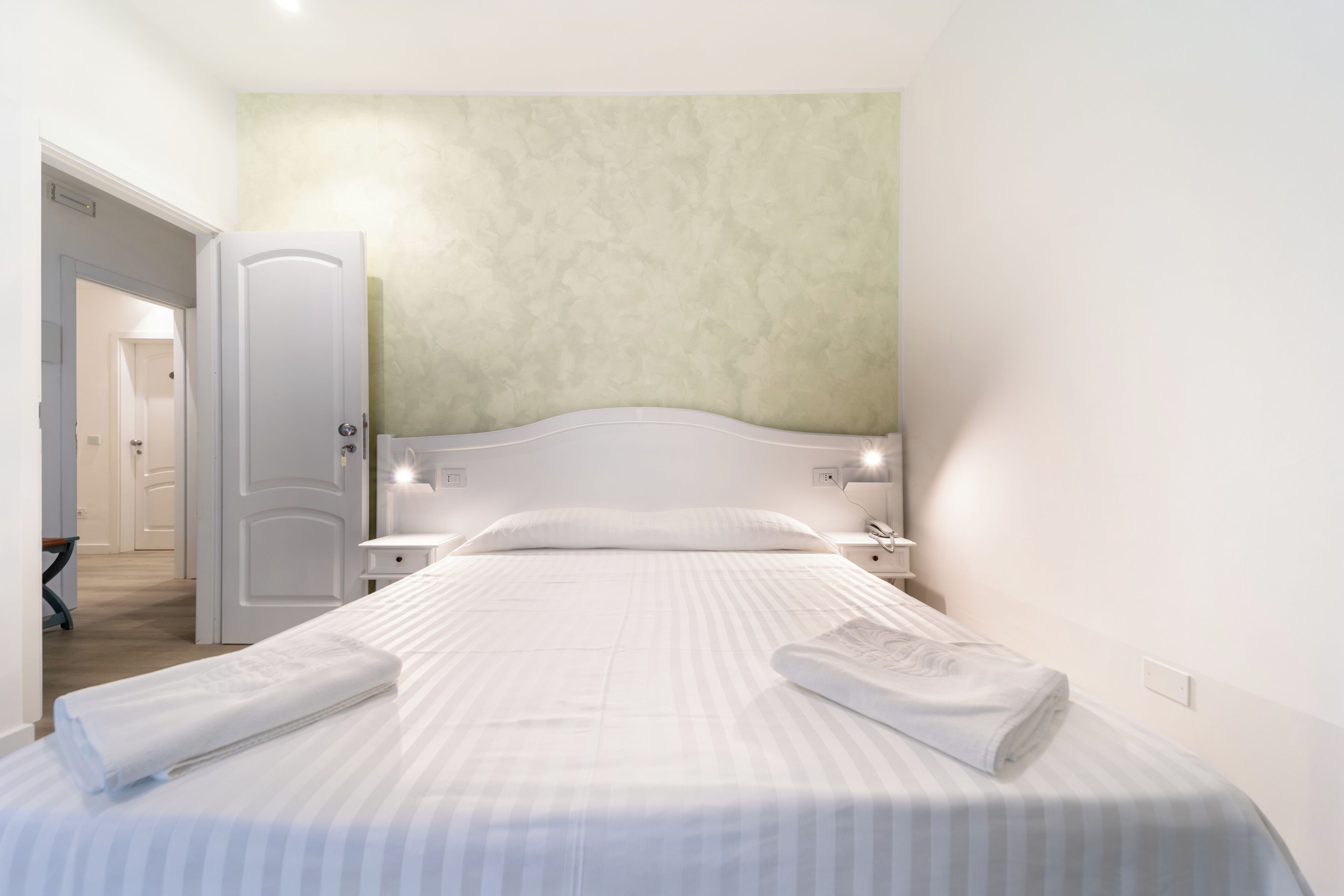 A hotel room with a bed, bedside tables, and a door to another room.