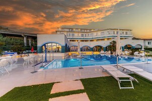 A hotel with a swimming pool, outdoor seating, and a view of the sunset.