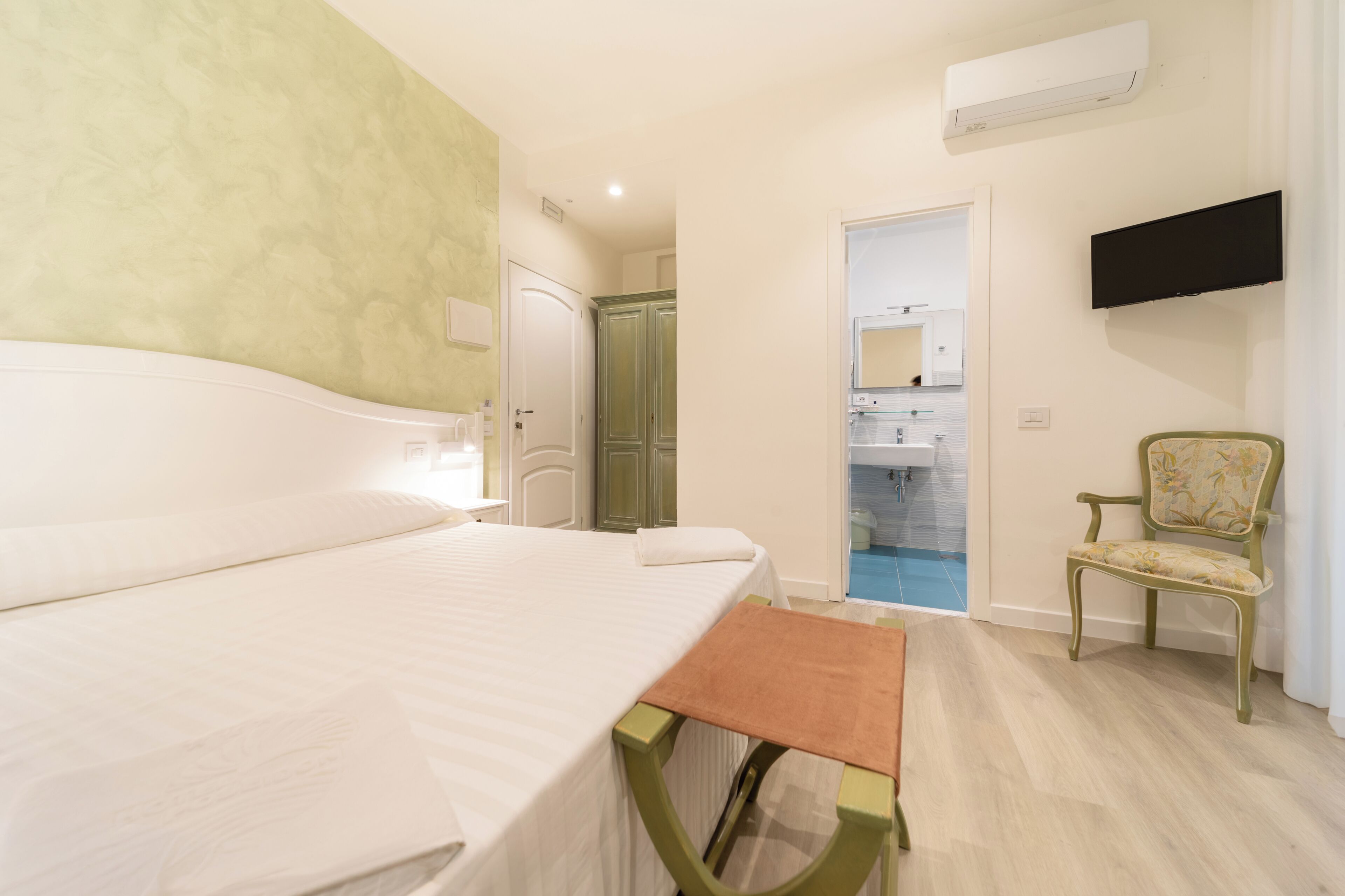 Ein Hotelzimmer mit Bett, kleinem Tisch, Sessel, Fernseher und einem Badezimmer mit Dusche.