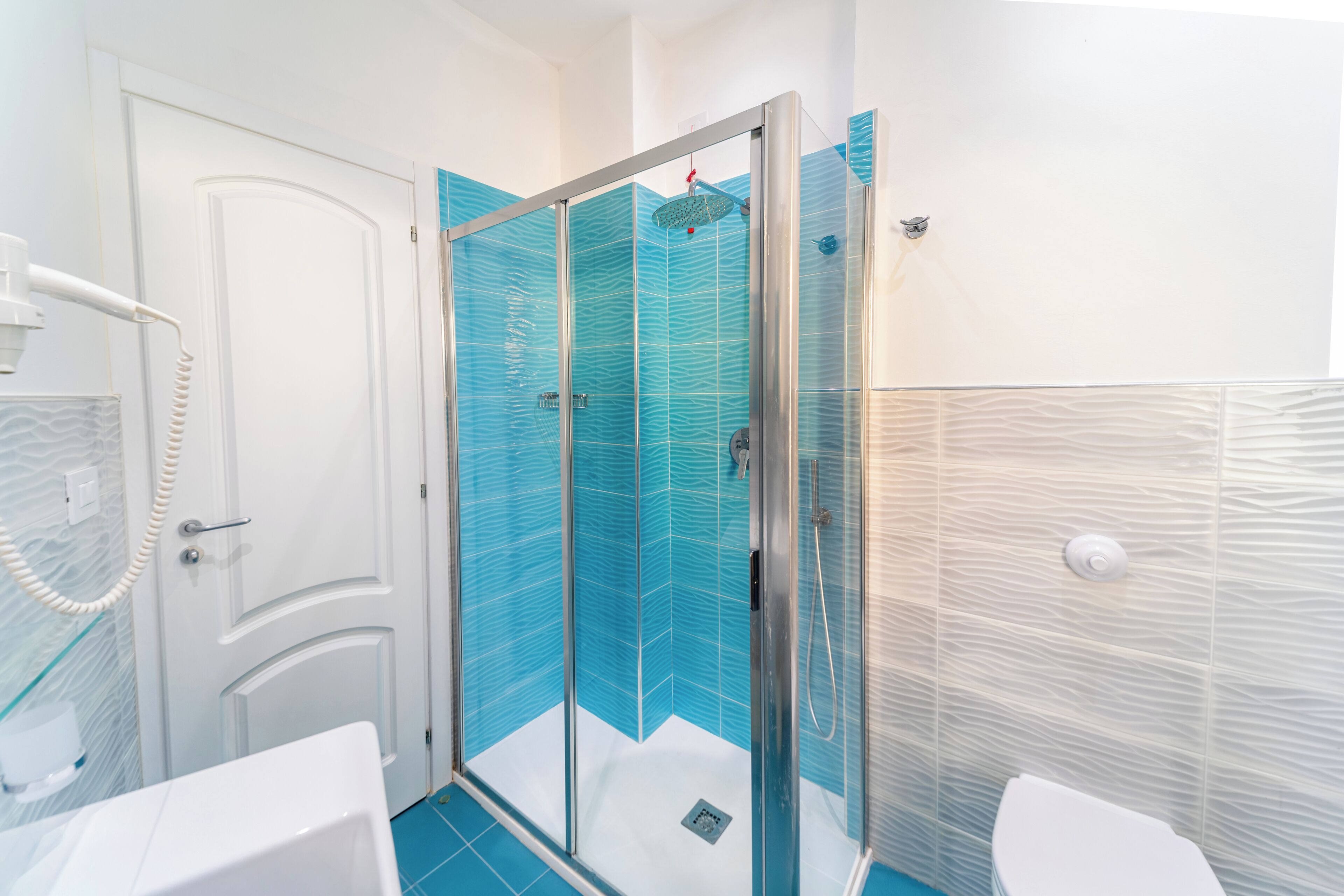 Een badkamer met een douchecabine van glas, witte muren en een wit toilet.