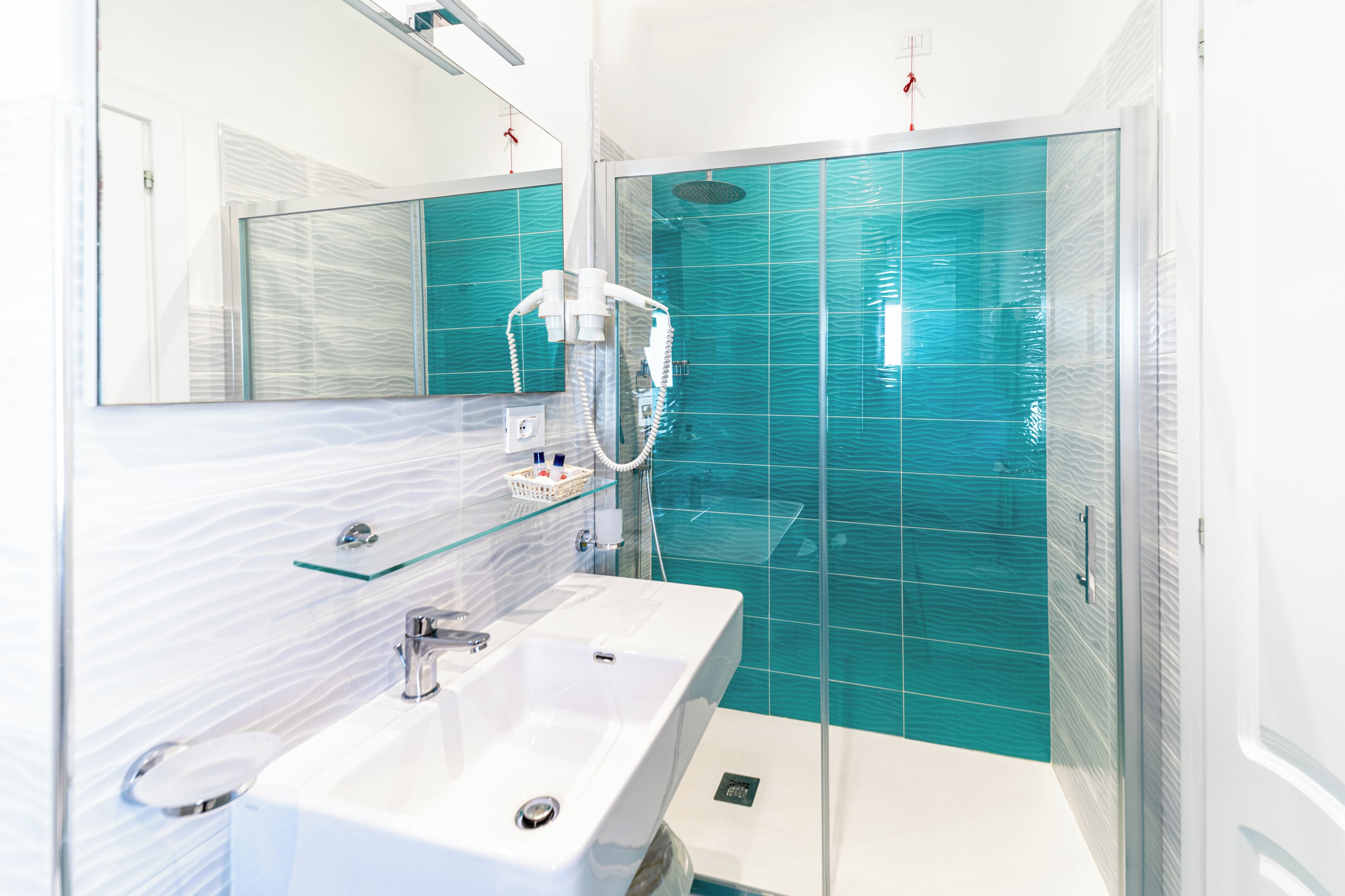 Une salle de bain moderne avec une douche à l’italienne en verre, un lavabo blanc et un grand miroir.