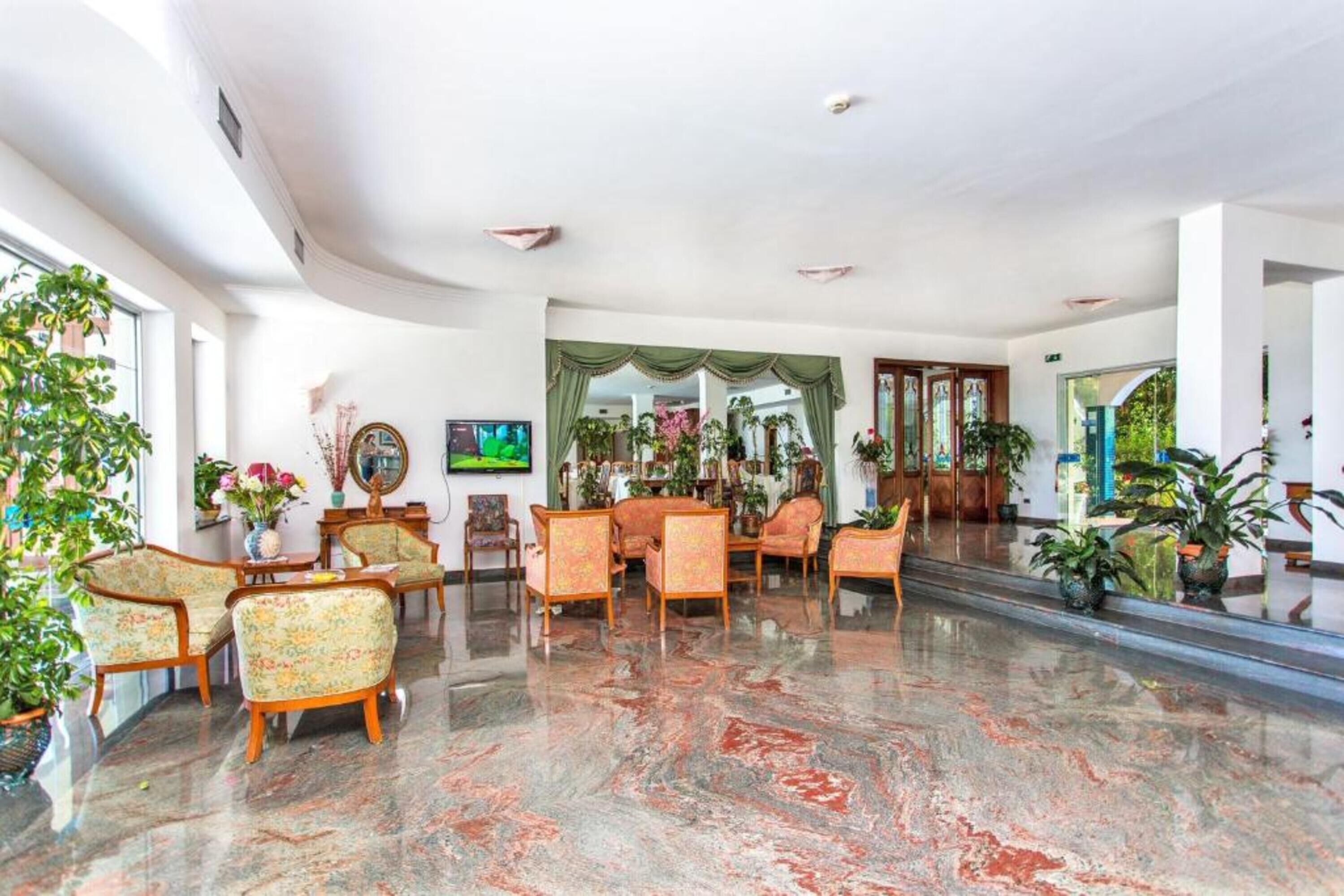 A spacious lobby with a marble floor, floral-patterned chairs, and a television.