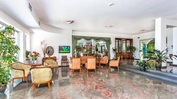 A spacious lobby with a marble floor, floral-patterned chairs, and a television.