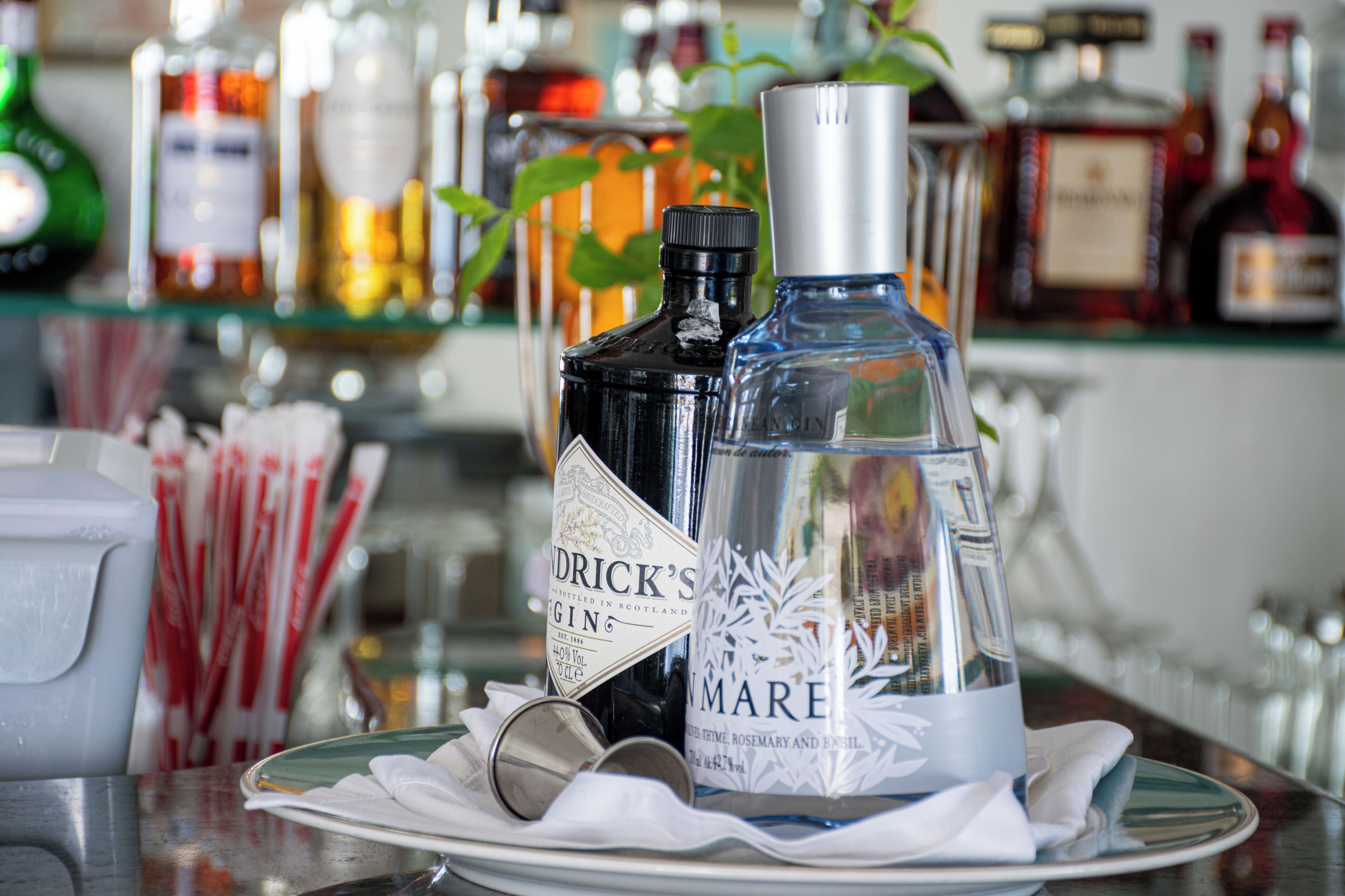 A bar setting with various bottles of liquor, including a prominent bottle labeled "Drick's Gin" and another labeled "Mare."