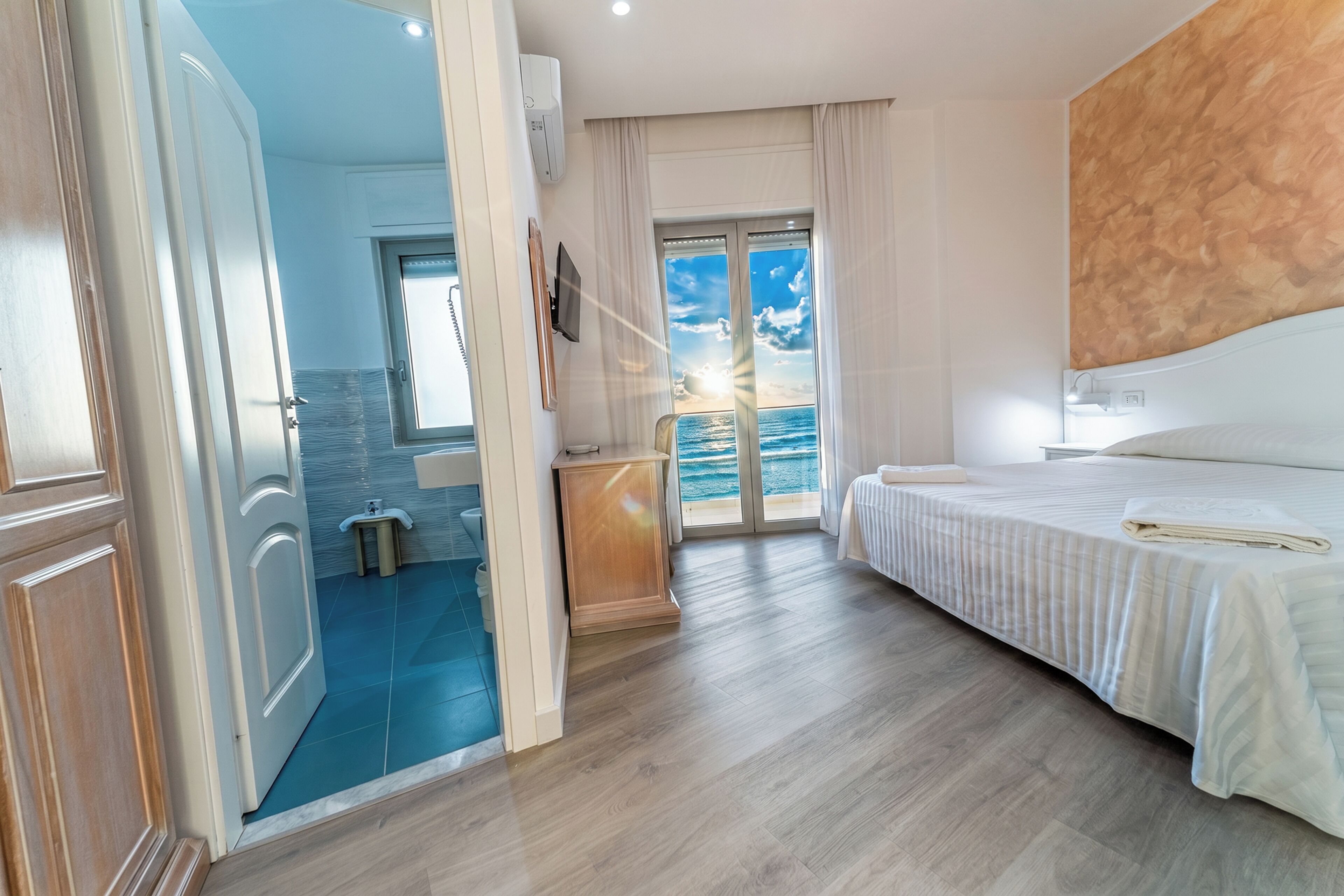 A hotel room with a bed, a bathroom, and a view of the sea.