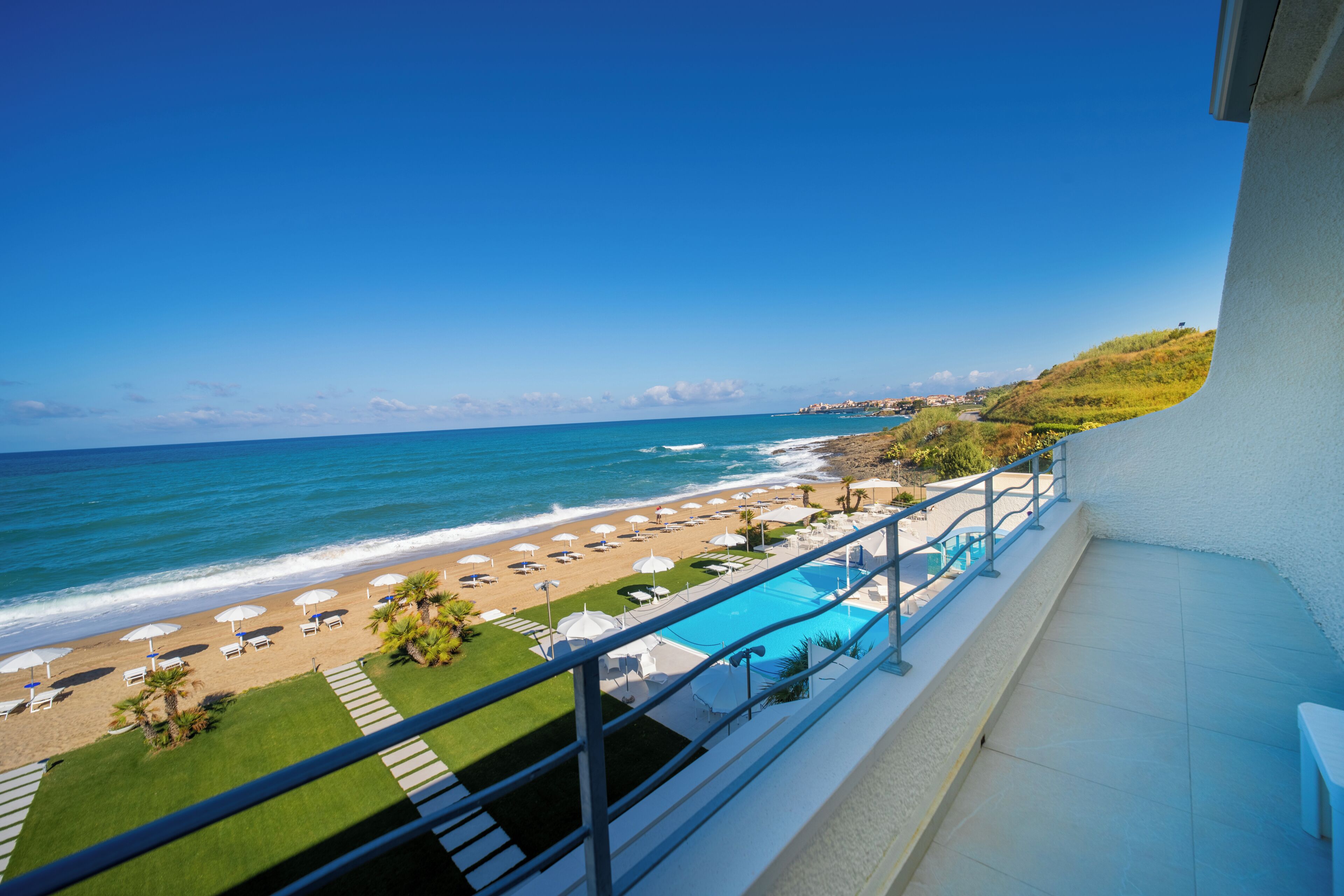 Ein Balkon mit Blick auf einen Strand, ein Schwimmbad und den Ozean.
