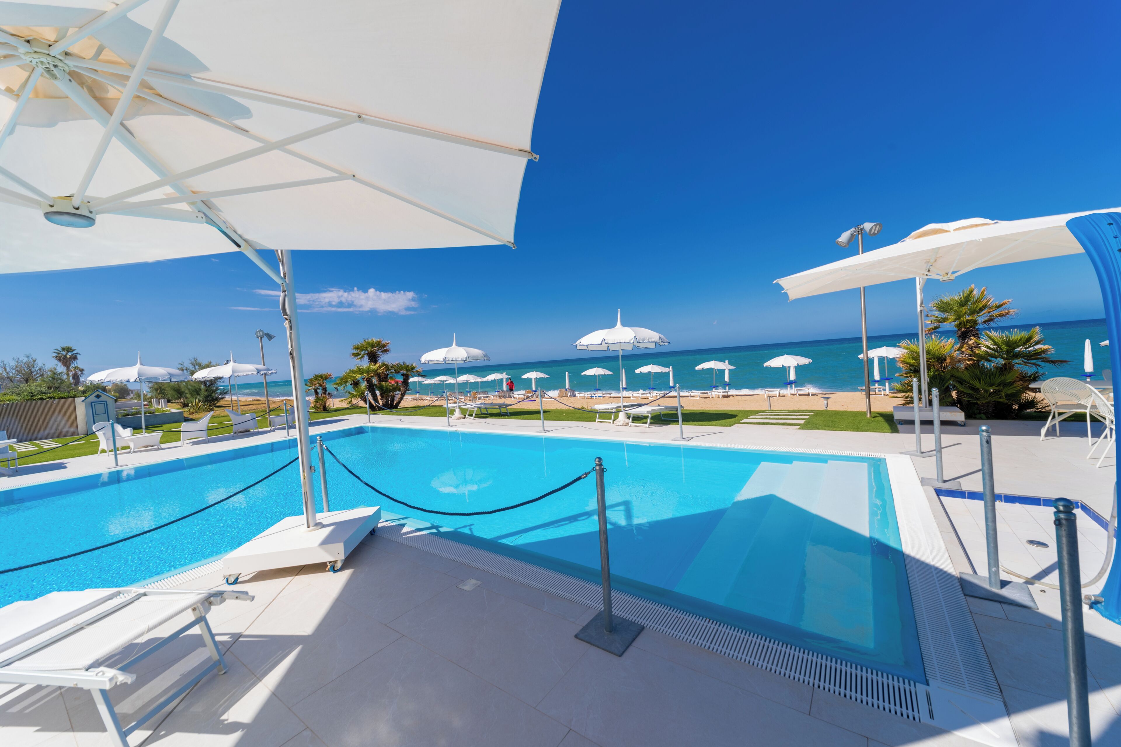 A swimming pool with sun umbrellas, lounge chairs, and a view of the ocean.