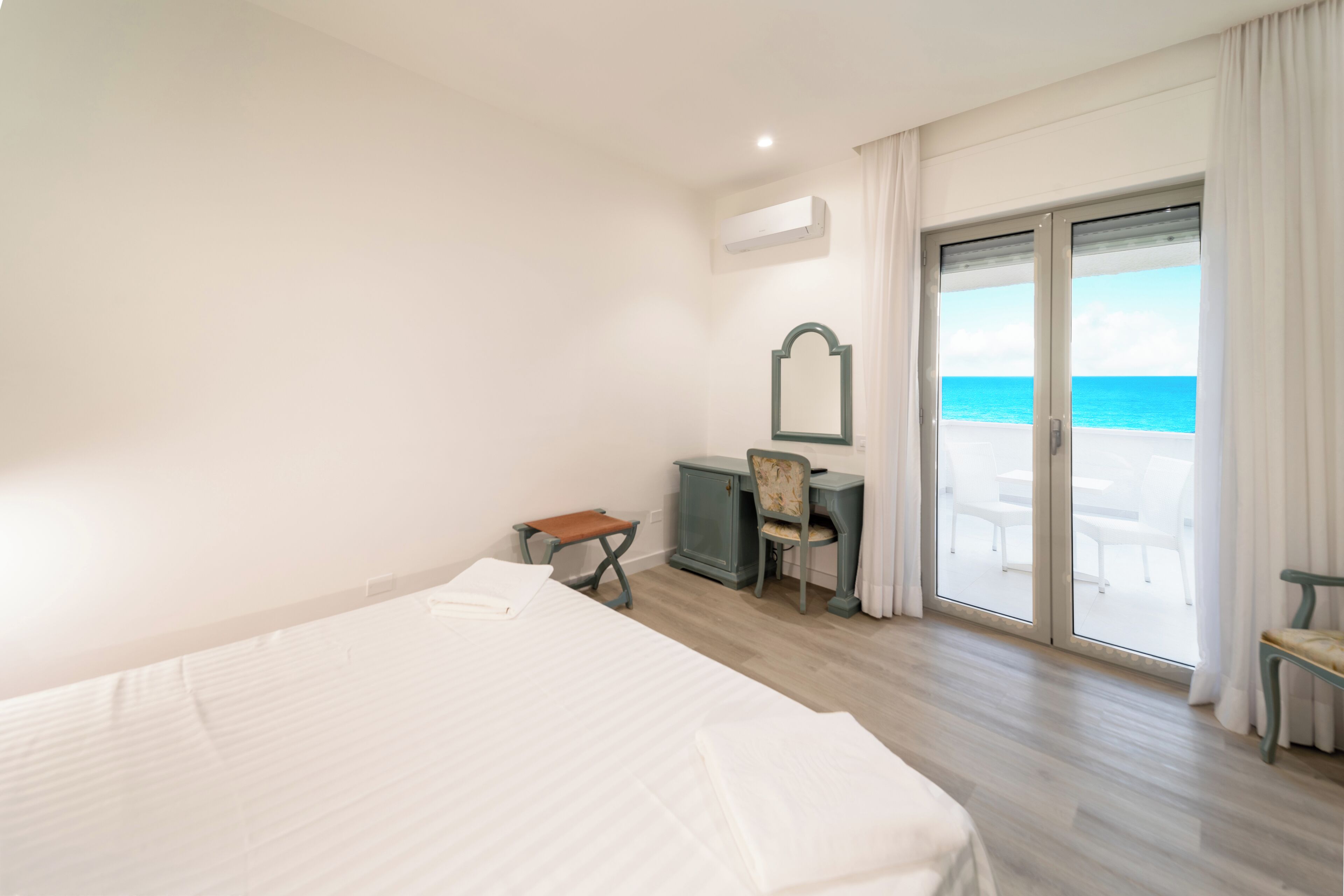 Une chambre d’hôtel équipée d’un lit, d’un bureau, d’une chaise, d’un miroir et offrant une vue sur l’océan grâce à une porte-fenêtre coulissante.