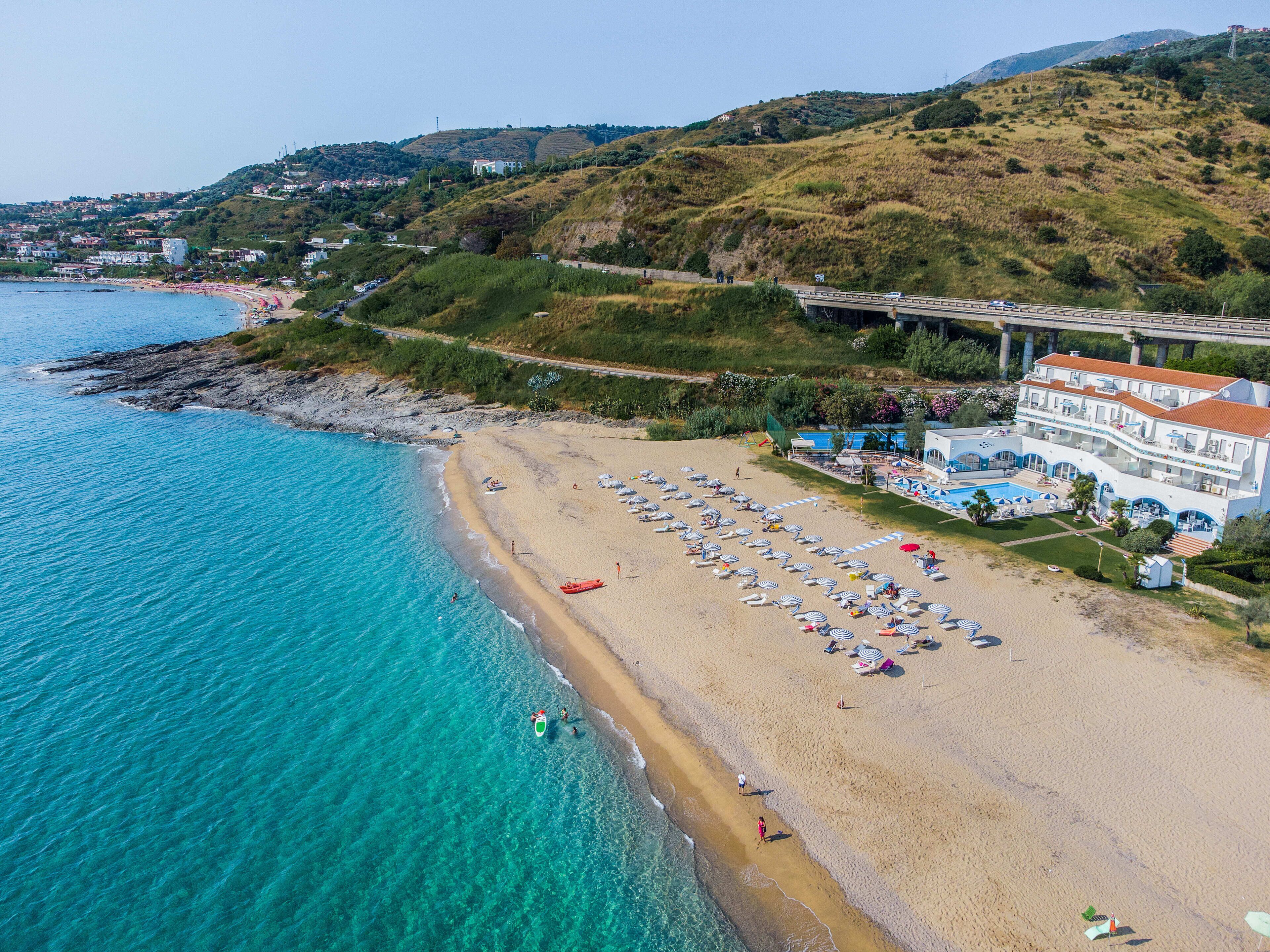 A coastal hotel with a beach, a pool, and a view of the sea.