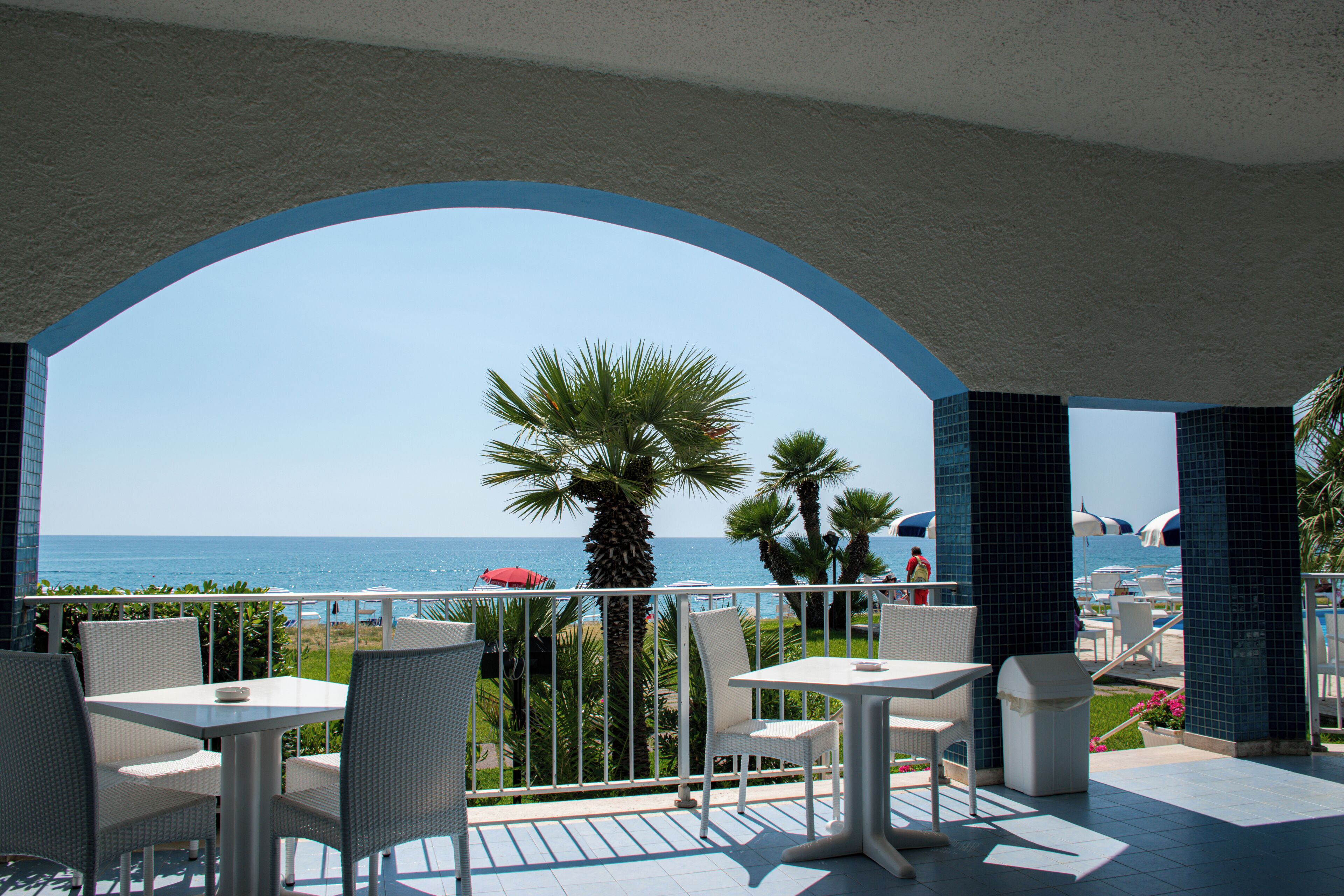 Una terraza con mobiliario de mimbre blanco, vista al mar y suelo de baldosas.