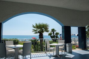 A terrace with white wicker furniture, a view of the sea, and a tiled floor. - Hotel Poseidon (Belvedere Marittimo)