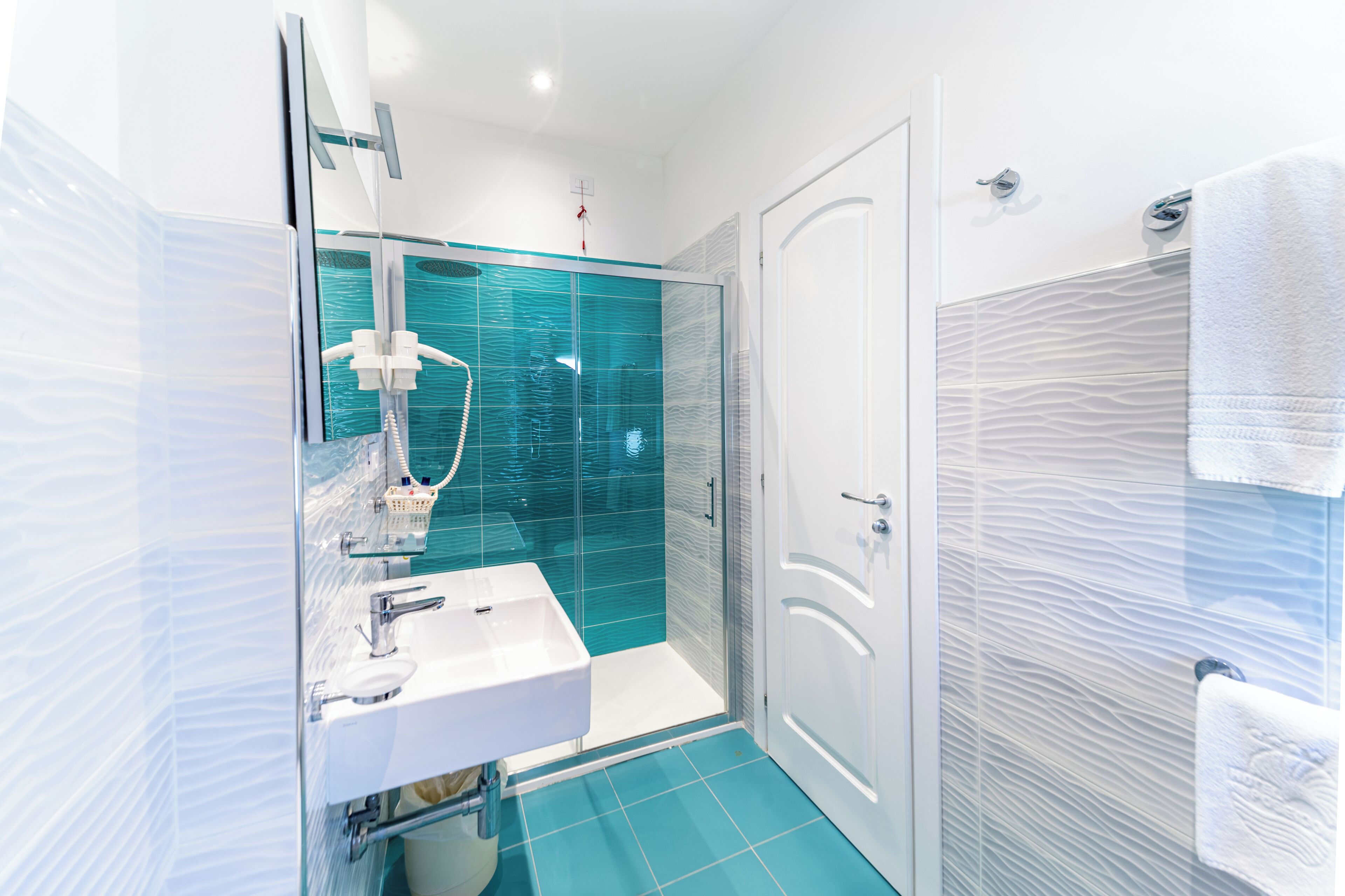 A modern bathroom with a glass shower enclosure, a white sink, and a towel rack.