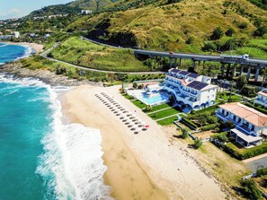 Una propiedad frente al mar, con playa, piscina y una carretera con vehículos.