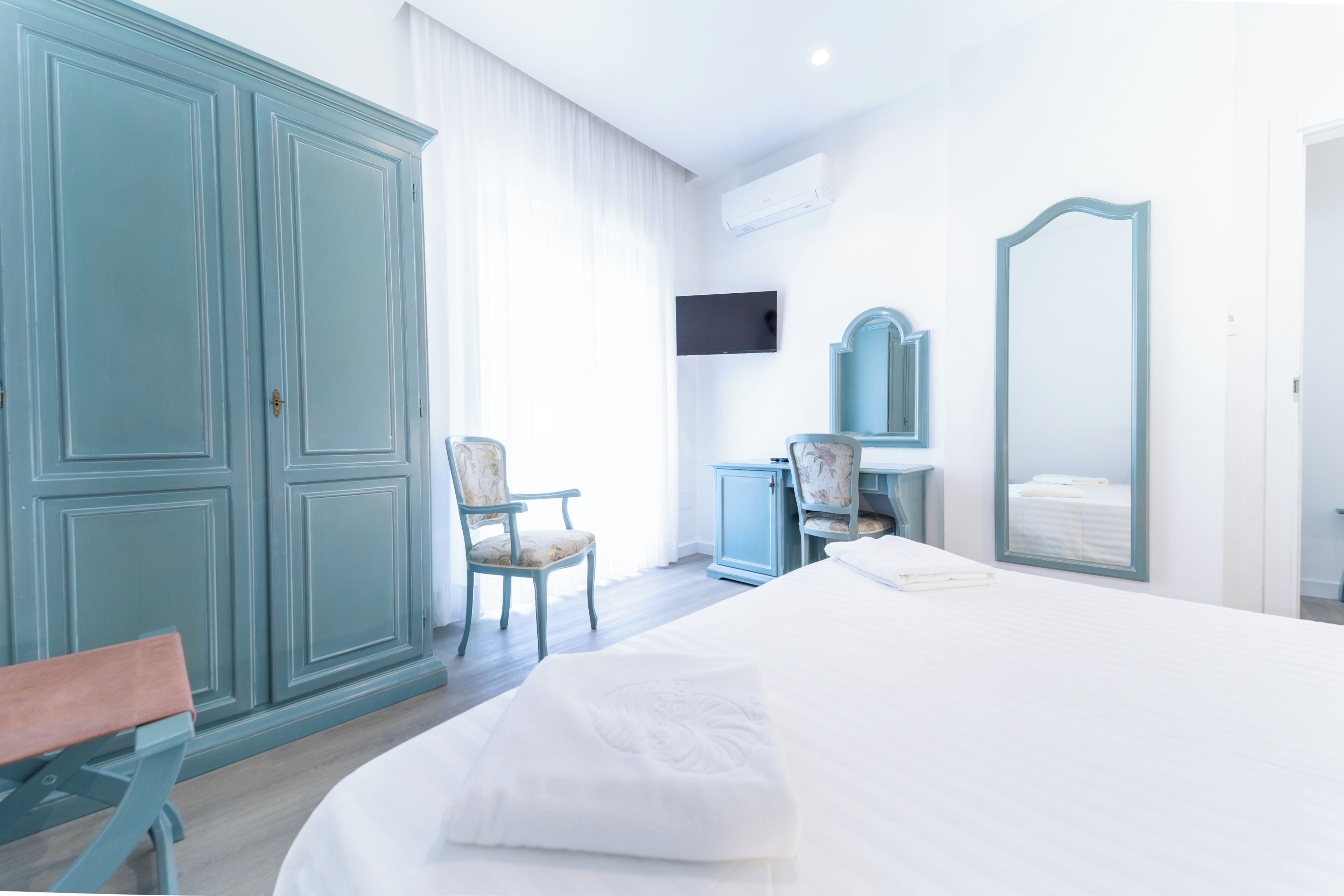 Una habitación de hotel con cama, una silla, un escritorio, un espejo y televisión.