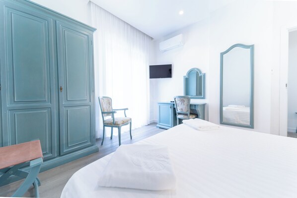 A hotel room with a bed, a chair, a desk, a mirror, and a television.