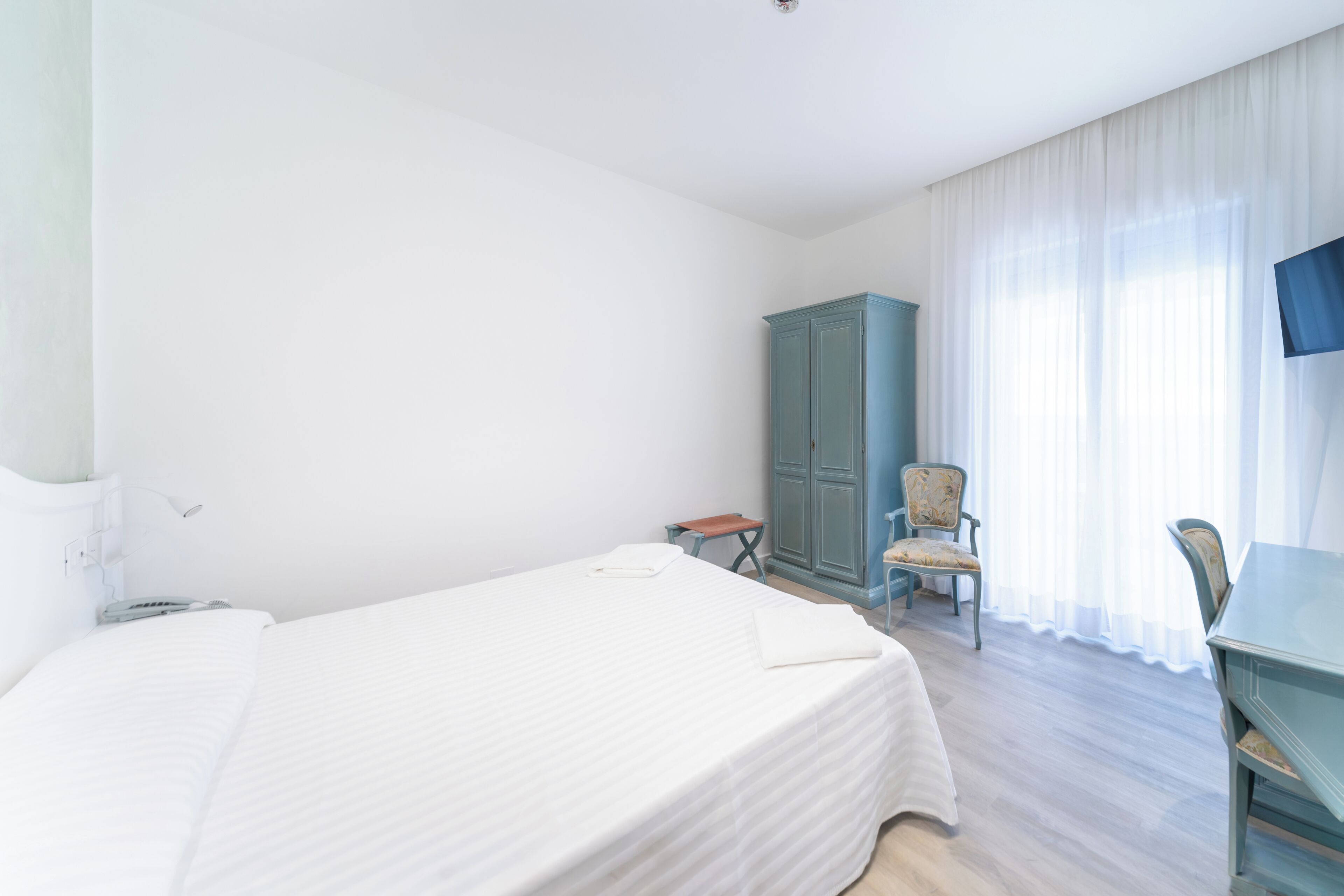Une chambre d’hôtel avec un lit simple, un bureau, une chaise, une armoire et un téléviseur.