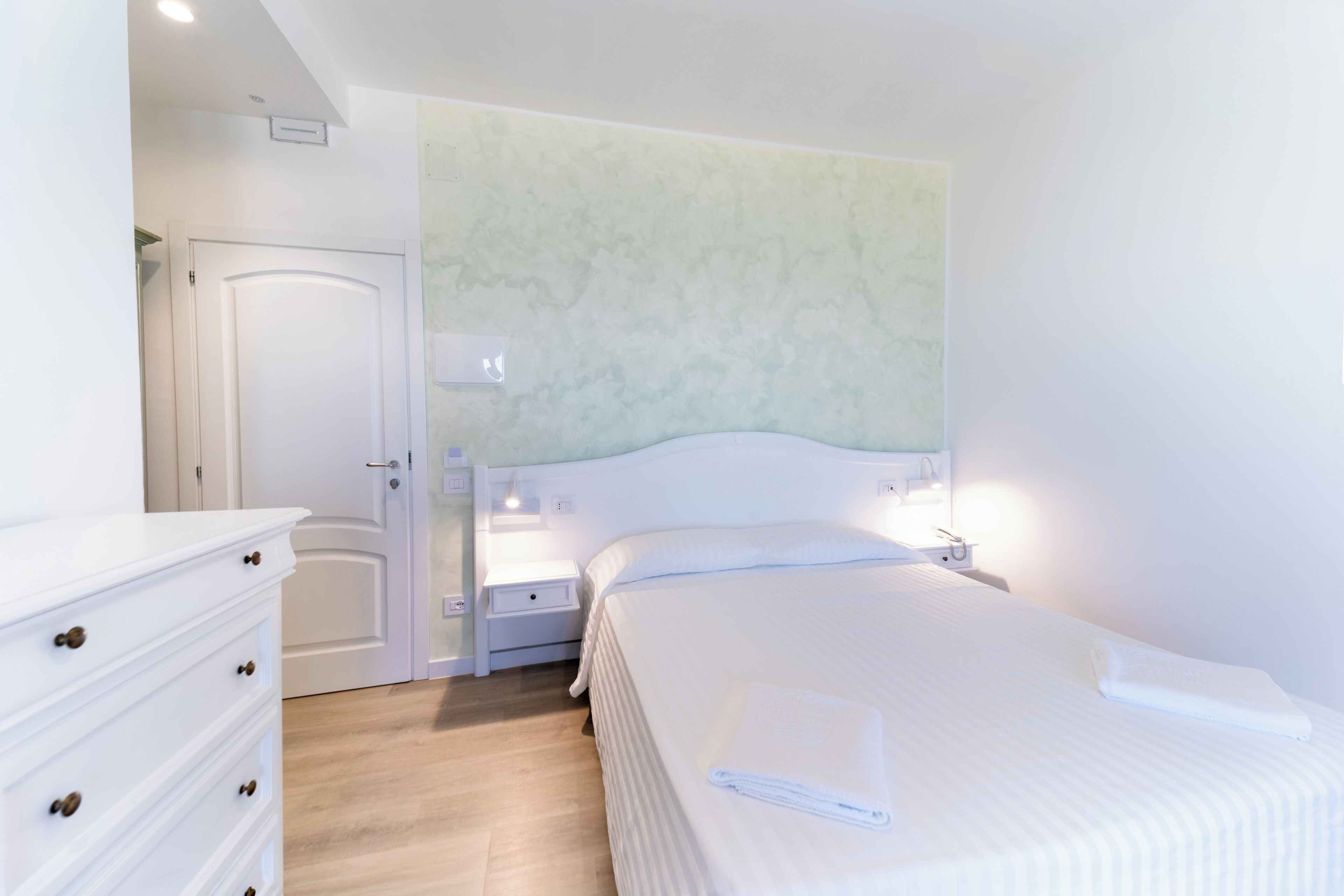 A bedroom with a bed, a nightstand, a dresser, and a door.
